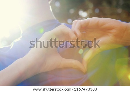 Teen making a love heart with their hands on their chest in the summer sunshine 
