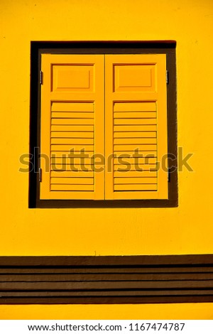 Vintage window with antique yellow shutters isolated on a yellow background wall in historic Little India, Singapore 