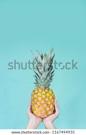 Holding a pineapple. Yellow nails. Girl hands. Girl with a pineapple in hands, in a blue background. Tropical and summer vibes. Minimalist photoshot. Pastel colors and colorful photoshoot.