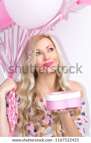 Portrait of a beautiful blond woman holding a gift, with pink and white balls. Pleases a gift, surprise. Celebration.