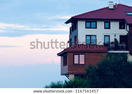 Old Bulgarian house with windows, a burgundy roof at sunset. House in the old town on a hill. Beautiful evening photo for background, cover, advertisement, travel site, brochure 