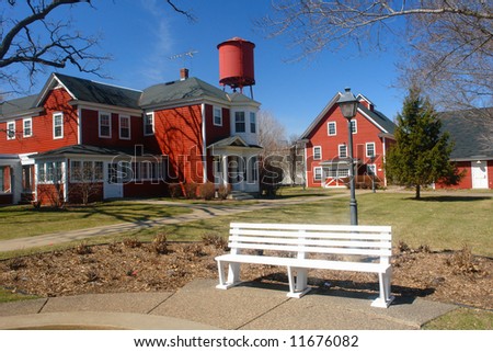   A picture of a white bench in front of red barn houses