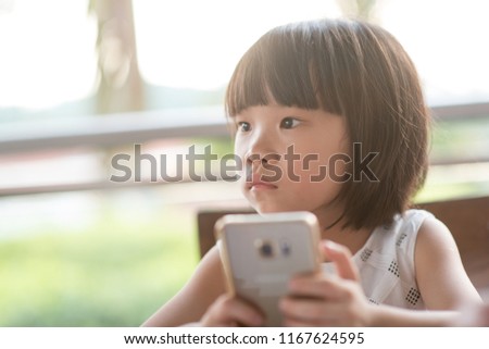 Asian child using smart phone at cafe. Natural light outdoor lifestyle.