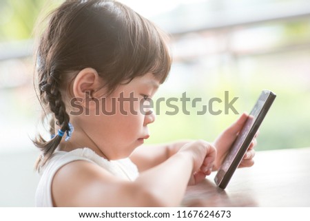 Little Asian girl addicted to smart phone at cafe. Natural light outdoor lifestyle.