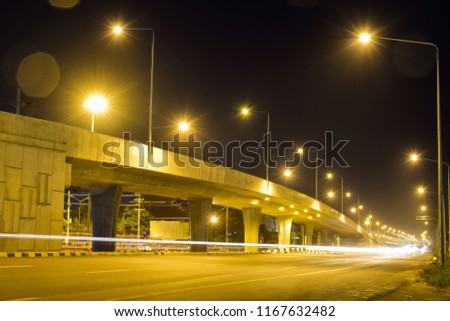 Light beam from vehicle pass through with golden light near to high way bridge. Night Traffic light