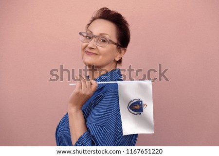 Massachusetts flag. Woman holding Massachusetts state flag. Nice portrait of middle aged lady 40 50 years old with a state flag over pink wall on the street outdoors.