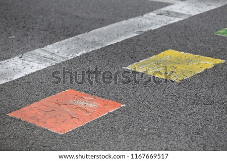 Close up outdoor view of many colorful traffic signs on a grey
asphalt road. Pattern of small squares drawn on the street. Graphic image with white, orange, green, blue and yellow geometric shapes. 