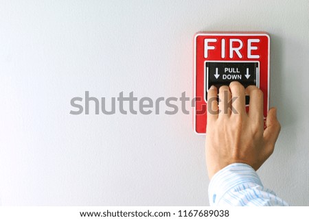 Hand of woman pulling fire alarm switch on the white wall as background for emergency case