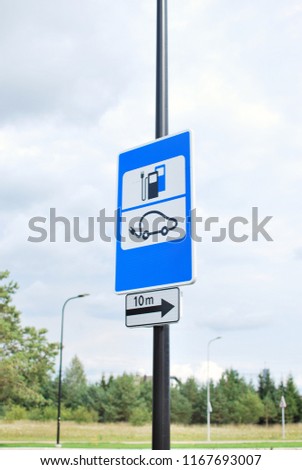 Electric vehicle recharging point sign. Charging station road sign with the sky and green trees on background.