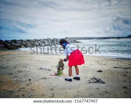 Baby girl is picking up the garbage by the sea. To reduce global warming is to help society.