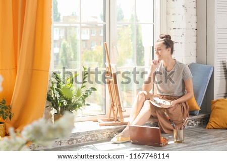Female artist waiting for inspiration near window in workshop