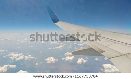 Airplane wing view out of the window on the cloudy sky background. Holiday vacation background. Wing of airplane flying above the clouds in the blue sky.
