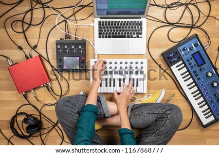 Woman making electronic music on laptop computer and digital instruments. Top view of young female producing modern indie music on synthesizer and digital controllers Royalty-Free Stock Photo #1167868777