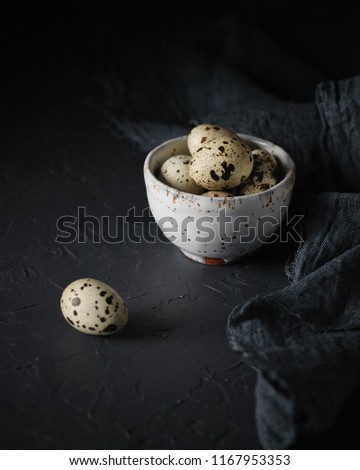 Fresh organic quail eggs in a vintage little ceramic bowl on dark grey background. Dark and moody picture. Low key. Close up, selective focus. Copy space