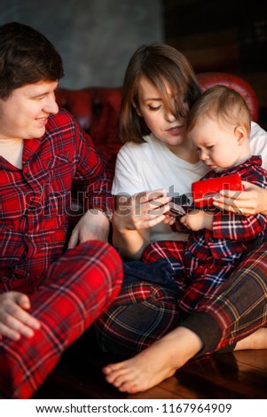 Picture of parents sitting together with their child on the floor. They are looking at him. Kid is playing on th phone. Dad is holding child on nap.