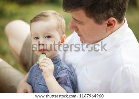 The child sits next to his father in the park. He is eating