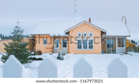 Beautiful Winter View of the Idyllic House with Gorgeous Backyard and a Fence. Soft Snow Falls on a Winter Day.