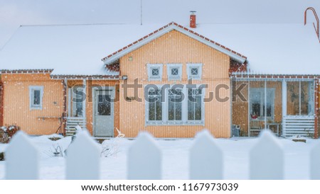 Beautiful Winter View of the Idyllic House with Gorgeous Backyard and a Fence. Soft Snow Falls on a Winter Day.