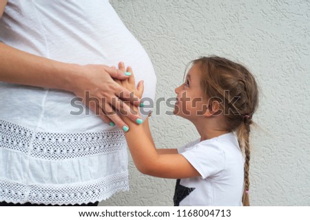 A adorable little girl holding her mothers pregnant stomach. 