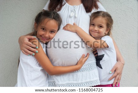 Two adorable little girls hugging their mothers pregnant stomach. 