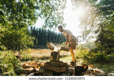 Picture of shirtless man who is chopping wood with an ax
