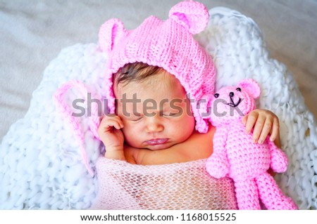 Sweet Caucasian newborn baby girl in a cute pink hat with ears hugging a teddy bear. Newborn photo session studio stock image. 