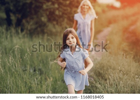 mom and daughter in beautiful dresses walk in field of beautiful summer weather