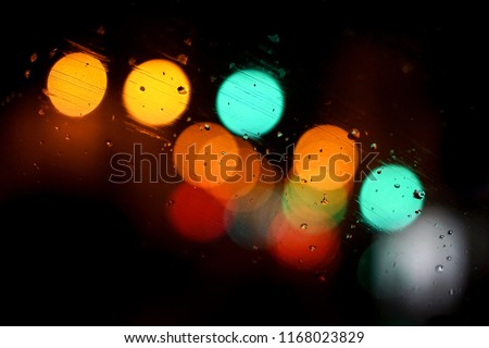 Artistic bokeh view of colorful street lights at night, through a car windshield, creating a pattern with rain water texture, as a fairy winter jazz and festive atmosphere, Paris city, France.