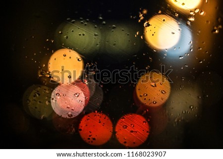 Artistic bokeh view of colorful street lights at night, through a car windshield, creating a pattern with rain water texture, as a fairy winter jazz and festive atmosphere, Paris city, France.
