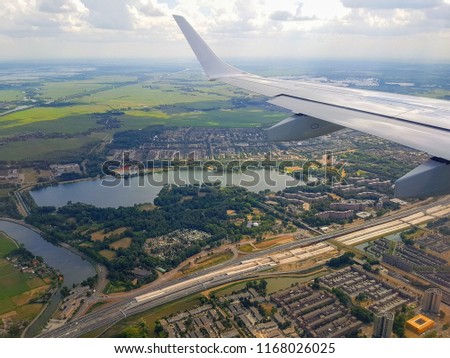Beautiful flight, skyline birds eye aerial panorama view of fields, houses, roads, roofs and cities of Netherlands, Amsterdam from aircraft board with plane wings during summer travel by plane