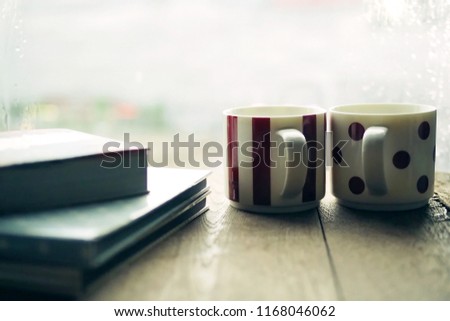 Romantic couple cups of coffee or tea on wooden table with some books over blurred background of window glass with raindrops and city view. (toned image, selective focus, space for text or article)