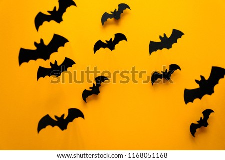 Black paper bats flying on yellow background. Halloween concept. Paper cut style. Top view