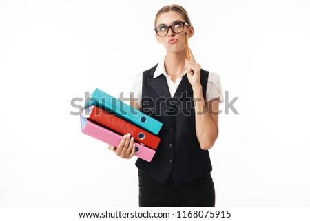 Young woman in black vest and eyeglasses playfully rolling eyes holding colorful folders and pencil in hands over white background