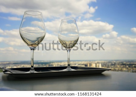 two empty vine glasses standing on black tray against blue sky with clouds