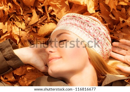 Picture of pretty woman sleeping outdoors, cute female laying down on autumnal foliage with closed eyes