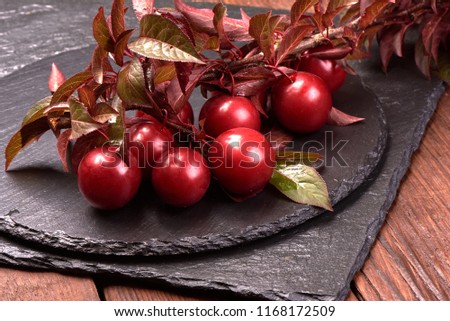 Red cherry plums fruits with leaves on a slate stone plate on a wooden rustic background