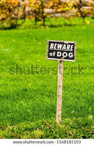 Beware of Dog sign posted in the green grass of an unfenced yard in a rural setting, background soft focus.