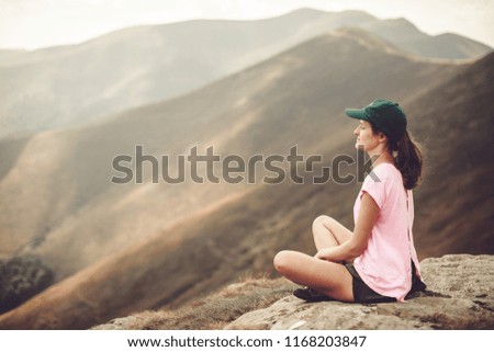 Young girl enjoying sunset and a view of the mountain ridge on peak of mountain. Tourist traveler sitting on viewing platform. Nature girl. Background 
 mockup for text.