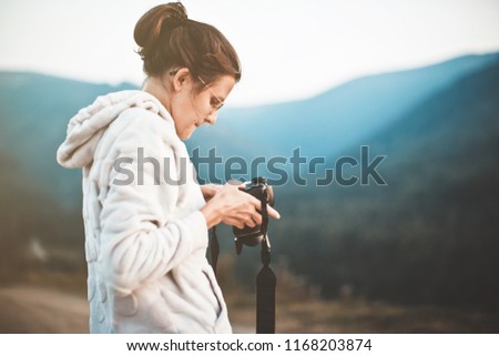 Young woman photographer holding camera and checking photo. Beautyfull, gorgeous background valley landscape view mockup for text. Girl with glasses. In the hands of the camera.