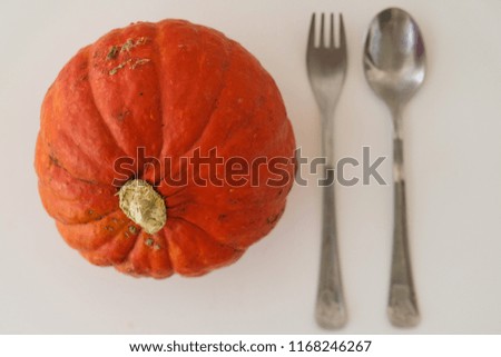 Symbol of Halloween and Thanksgiving day, big orange pupkin, lays at table with fork and spoon beside. Top view. This is delicious vegeterian meal, element of raw and healthy diet.