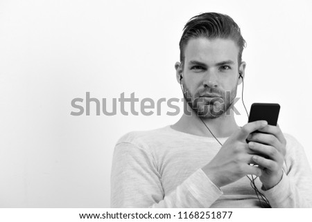 Guy with beard holds MP3 player and wears earphones on white background. Man with smiling face with telephone. Entertainment and musical concept. Macho with headphones and cell phone listens to music