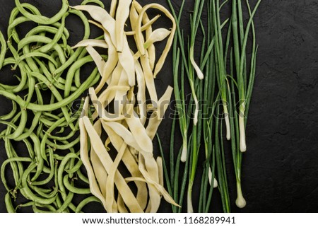 Healthy raw summer vegan vegetables, green and yellow beans, onions on dark stone background. Healthy food, clean eating, top view, flat lay, copy space
