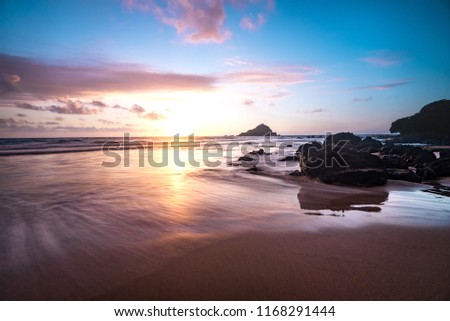 Relaxing Tropical Island Paradise of Colorful Pastel Sunrise Sky at Dawn with Sun Coming Over Ocean Horizon on Sandy Beach with Mountain Background and Pink Clouds on Maui Hawaii
