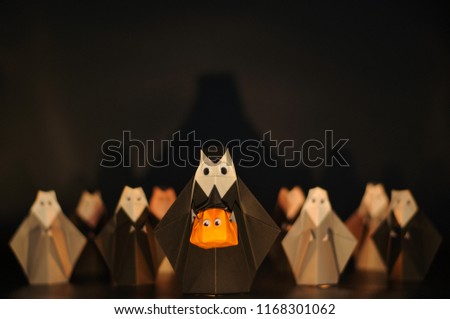 The Halloween origami (or Paper folding) Nun holding pumpkin head jack-o-lantern made from folded paper with many nuns at the back isolated on black background with space for text.