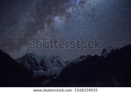 The Milky Way stretches across the sky in the Cordillera Huayhuash, high in the Peruvian Andes. A snow capped peak is visible below the bright stars of the galaxy. Long exposure.