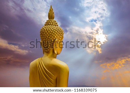 Close up big golden buddha statue with sunlight rays twilight sky background.