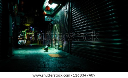If a child stays curious, he will continue to explore and discover. In the image, a boy squats down and peeps into a small gap. He is curious what is inside. The street is dark as shops closed. Royalty-Free Stock Photo #1168347409