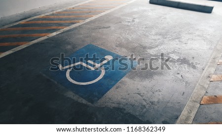 Blue handicap parking spot sign on concrete floor between caution area with gradient light from outside the building. 