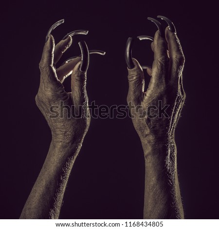 Closeup view of two female old scary mystic hands with long black nails on fingers of witch zomby demon or devil on halloween holiday character in studio indoor on dark background, square picture