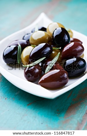 Marinated olives with rosemary in a small ceramic bowl. Organic kalamata, black and green olives. Symbolic image. Concept for a tasty and healthy appetizer. Rustic wooden background. Close up.